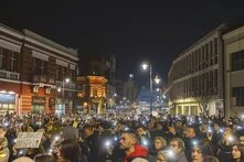 Photo: Night protest in a Serbian city, large crowd fills the street, many hold up phones with flashlights, one sign reads "Don't lie to my grandma!" in Serbian Cyrillic.